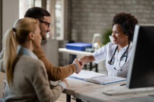 *Check-up Executivo: saúde estratégica para líderes e empresas*. 2 happy couple shaking hands with black female doctor after consultations clinic focus is doctor